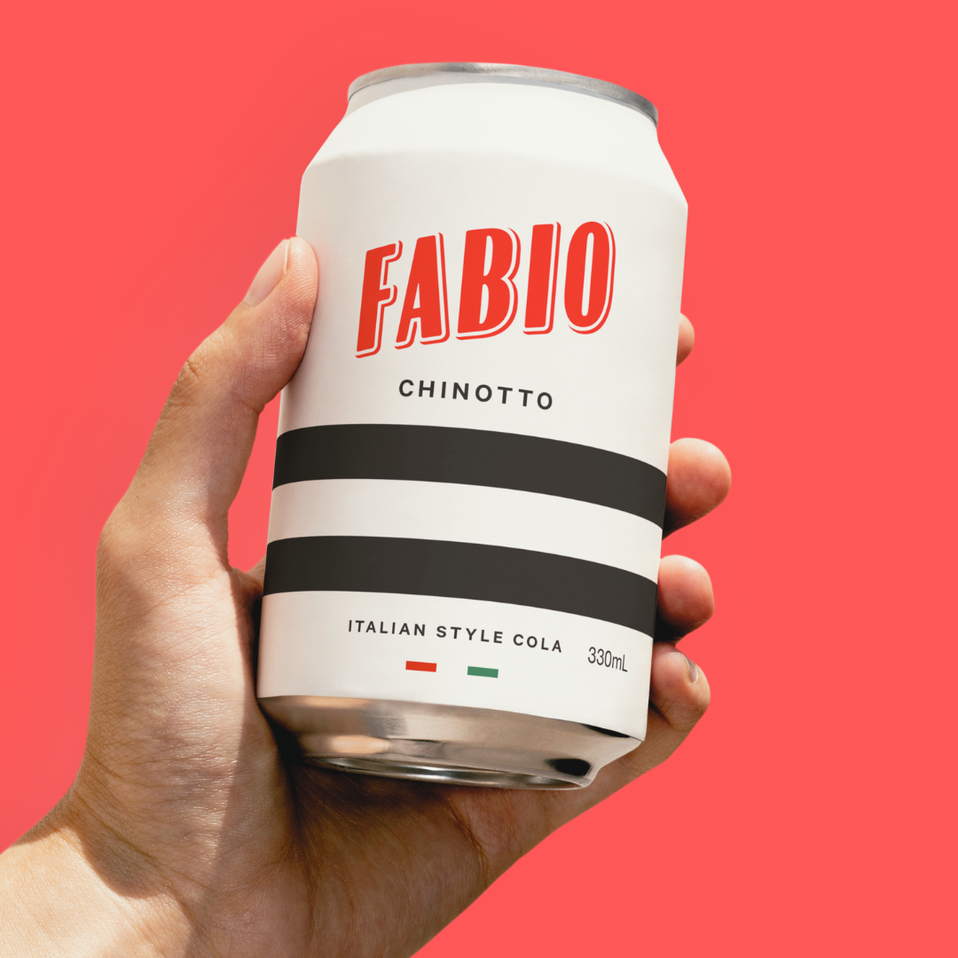 Hand holding a can of Fabio Chinotto Italian Style Cola against a red background